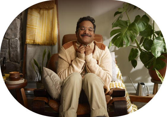 A man smiling sitting on a brown chair. He looks warm and cozy.